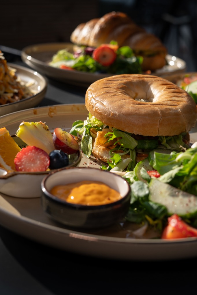 Herzhaft gefüllter Bagel mit cremigem Ei, Salat und Obstschale